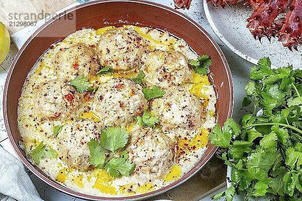 Food  CRABMEATBALLS crab meatballs in white creamy sauce in red pan  whole king crab  cilantro  lemon and white wine on white background