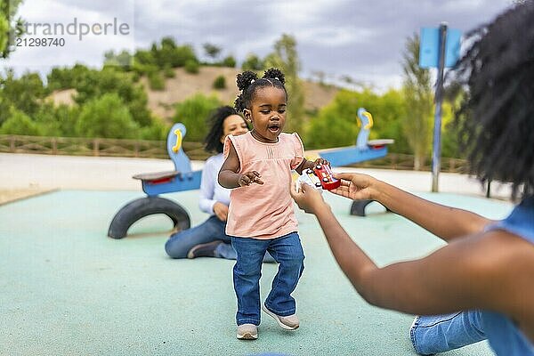 Baby african girl walking to her mother to pick a toy in a public park