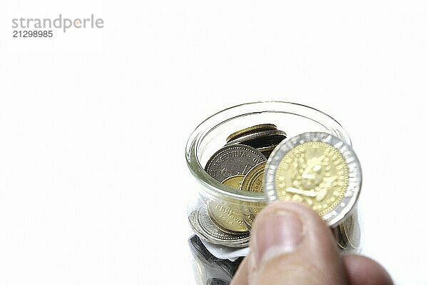 Glass jar with many Coins  hand holding a coin against white background