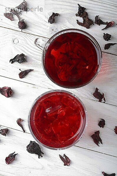 Top view at two tea cups with ice and dry hibiscus petals on white wooden table background