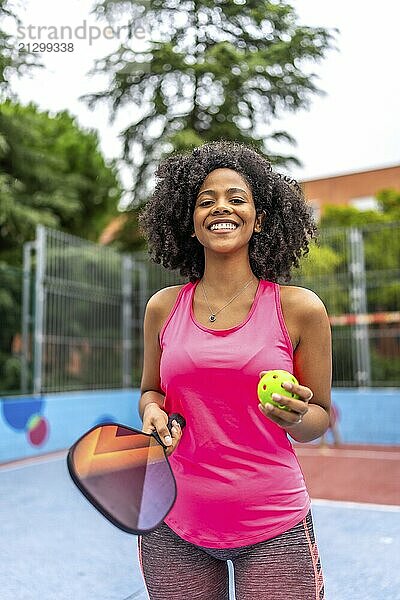 Vertical portrait of a latin female pickelball player standing smiling at camera in an outdoor court