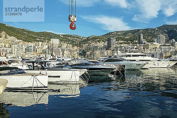 Awe Morning view on boats and yachts (sailboats) in Hercule port and buildings of Monaco in distance. Sun shiny in reflections. Crane above for lifting boats (nautical vessels) . Several crane machinery among buildings of Monaco hotels and casino buildings. Mountains above buildings  Fantastic summer for recreation  vacations and travel