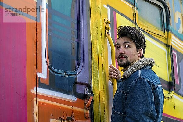 Portrait of a stylish handsome young man with a denim wool jacket outdoors on a train. A man wearing a denim wool jacket and a hat  looking at the camera