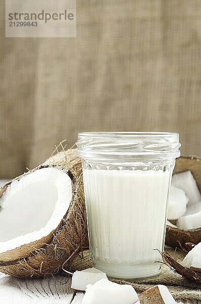 Mason jar of milk or yogurt on hemp napkin on white wooden table with coconut aside