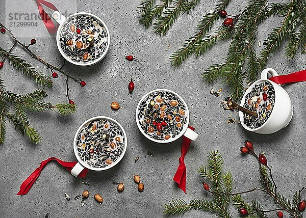 Four white cups filled with nuts  berries and seeds  decorated with twigs and red bows  on a grey background. Making food cups. Handicraft  crafting with children. Step by step instructions