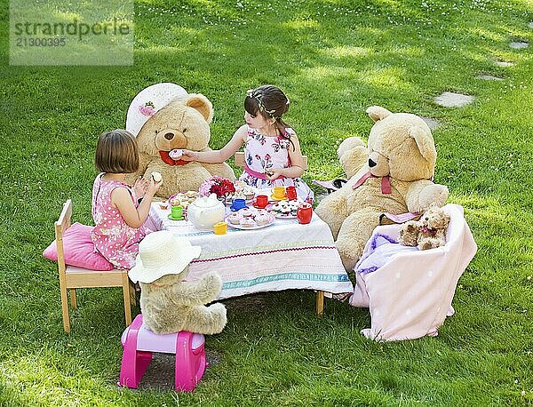 Elevated view of two young girls playing Teddy Bears Picnic in their back garden themes of imagination daydreaming playing