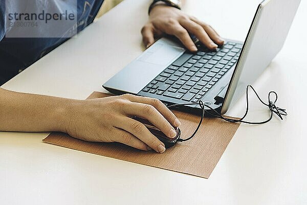 Young man working with laptop  hands on notebook computer and mouse. Focus on hand on mouse  blurred background. Student working at home