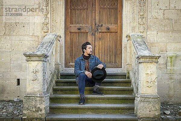 Portrait of a young man sitting against a beautiful old medieval cathedral door. A man in front of a an old architecture church entrance door in Alba Iulia  Romania  Europe