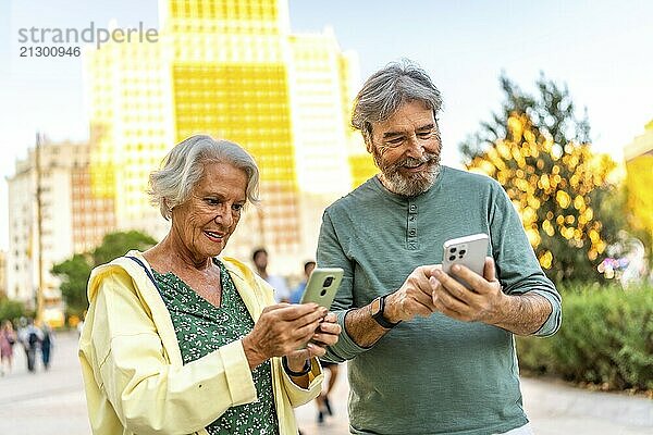 Caucasian modern senior couple using mobile phones standing in the city