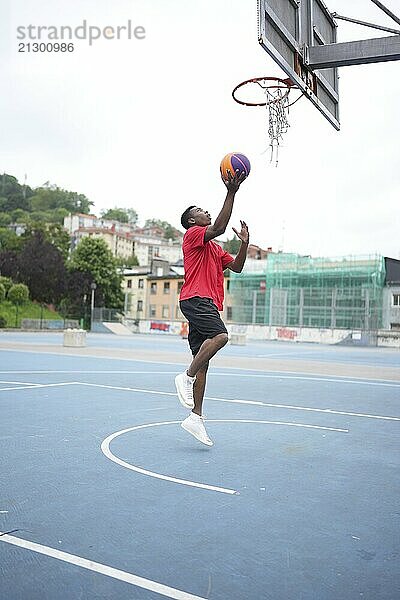 Vertical photo of a ypung african male basketball player jumping to throw a ball