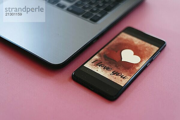 Valentines day sale background with heart illustration with the words I Love You on smartphone screen mockup on pink background with laptop