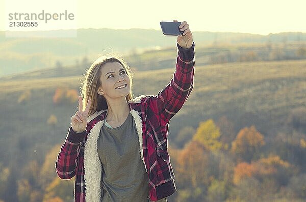 Young happy woman having fun outdoors taking selfie standing on the top of the hill. Backpacking tourism concept