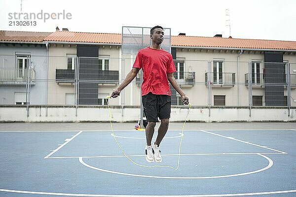 Young African American man wearing sports clothing is jumping rope in an urban basketball court