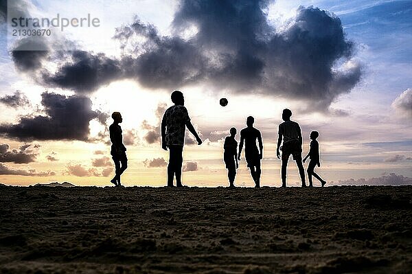 Group of people enjoying a football match on the beach at sunset  silhouettes against a backdrop of clouds  La Digue  Seychelles  Africa