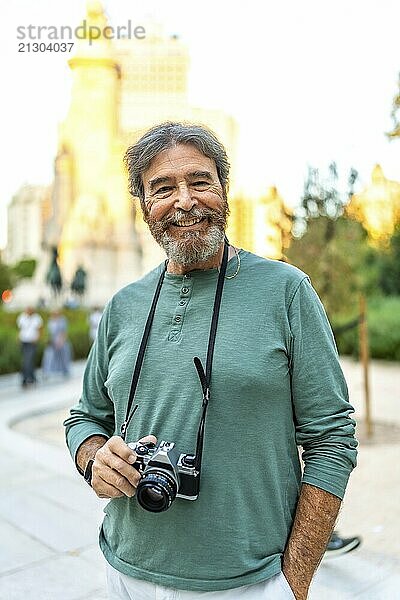 Vertical portrait of a smiling senior retired man holding camera while visiting a city