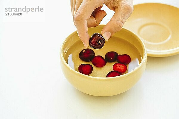 Young hand taking cherries in bowl with water against white background. Horizontal composition  space for copy