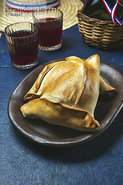 Food  Food  Tipical Chilean baked empanadas de pino y napolitano on clay plates with wine. Dish and drink on 18 September party Independence day Chile  blue background