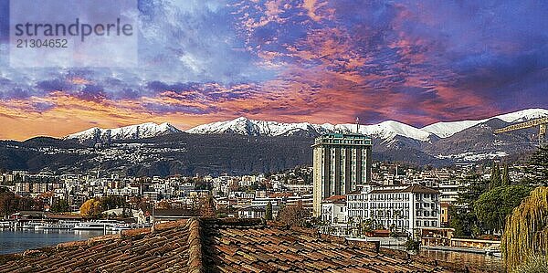 Sunset in Lugano and snow-capped mountains and forest behind. Cityscape and lower left cornet and autumn leaf color of trees in sunny day of begin of winter. Construction crane  at right side