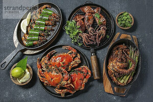 Food  Set of Seafood Dishes. Crabs  octopus  squids and tiger shrimps on cast iron pans and plates on a black background. Top view