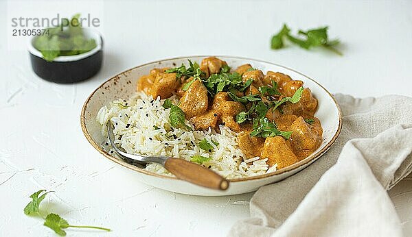 Traditional Indian dish chicken curry with basmati rice and fresh cilantro on rustic white plate on white concrete kitchen table  close up with selective focus. Indian dinner meal  food photography