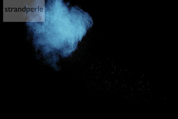 Blue color powder explosion cloud on black background.Closeup of Blue dust particles exhale on dark background