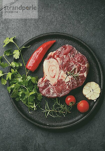 Food  Raw fresh ossobuco con herbs  garlic and chile pepper on black plate. Dark background