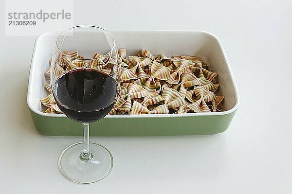 Close up of a dried fresh multicolored pasta and glass of red wine on white background