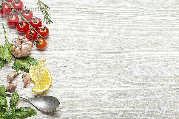 Healthy food ingredients composition with fresh cherry tomatoes  herbs  garlic cloves  lemon wedges and spoon on white wooden rustic background  overhead shot with copy space  food photography  food photography