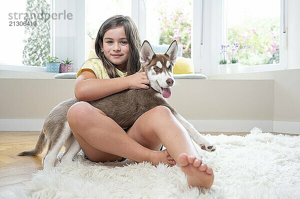 Smiling girl and her Siberian Husky puppy on carpet at home.