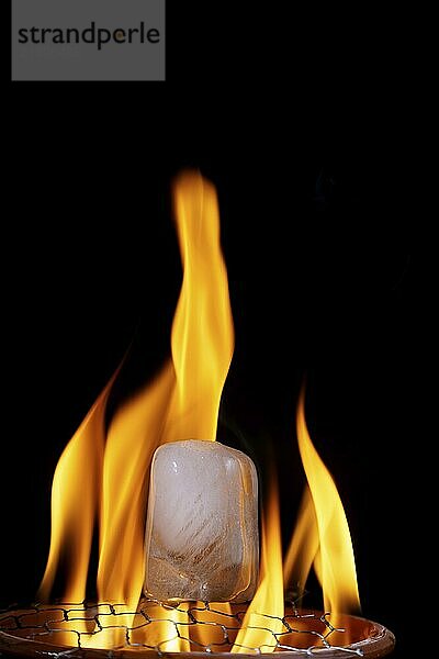 Ice cube burning in fire isolated on black background with copy space