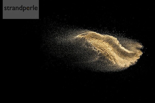 Golden sand explosion isolated on black background. Abstract sand cloud. Golden colored sand splash against dark background. Yellow sand fly wave in the air