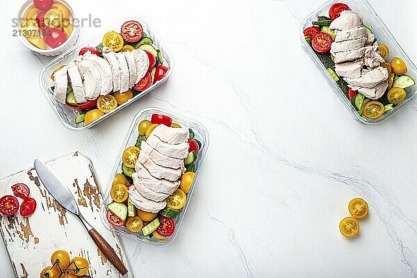 Healthy meal prep for lunch  diet boiled chicken fillet with vegetables salad in lunch boxes containers top view on white marble kitchen table background with knife and cutting board. Space for text  food photography  food photography