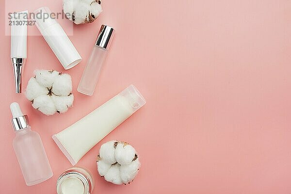 Glass and plastic cosmetic bottles on pink background with cotton bolls. Copy-space for text