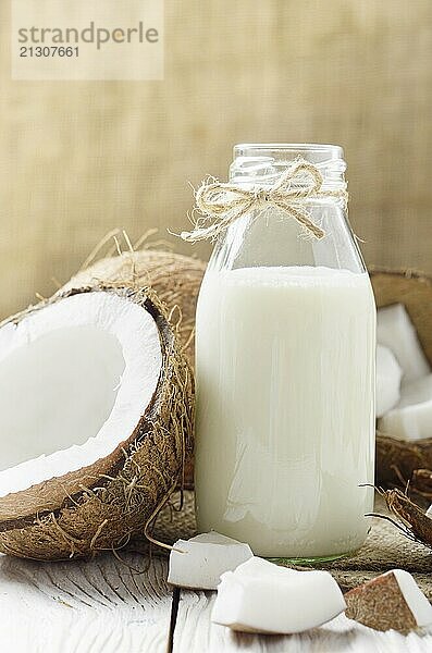 Glass bottle of milk or yogurt on hemp napkin on white wooden table with coconut aside