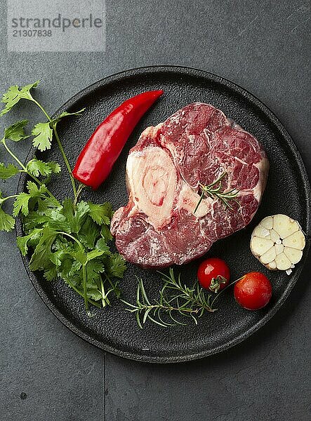 Food  Raw fresh ossobuco con herbs  garlic and chile pepper on black plate. Dark background