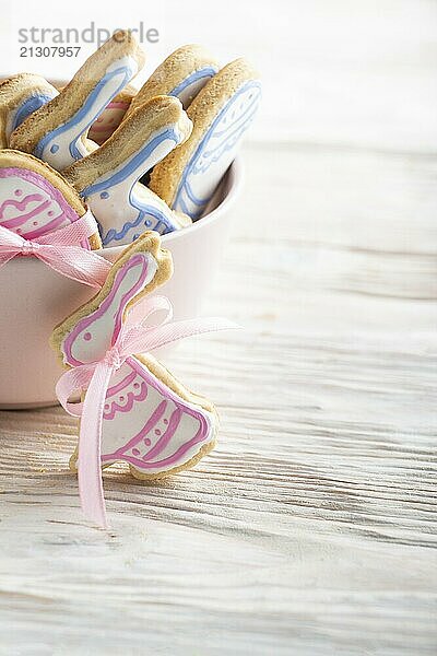 Pink clay bowl full of homemade Easter cookies in shape of bunny on white wooden kitchen table. Place for text