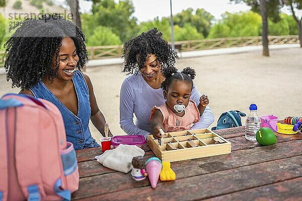 African granny  mother and girl playing with toys in a picnic table in the park