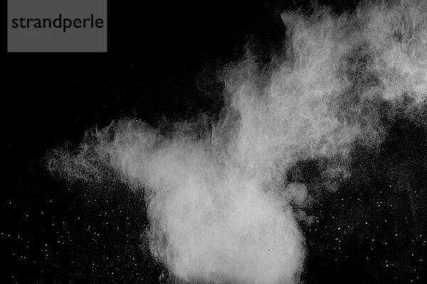 Freeze motion of white dust particles on black background. White powder explosion