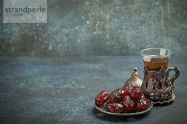 Breaking fasting with dried dates during Ramadan Kareem  Iftar meal with dates and Arab tea in traditional glass  angle view on rustic blue background. Muslim feast  space for text  food photography  food photography