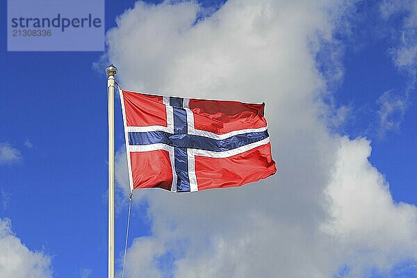 Flag of Norway against blue sky and white clouds. The flag of Norway is red with an indigo blue Scandinavian cross fimbriated in white