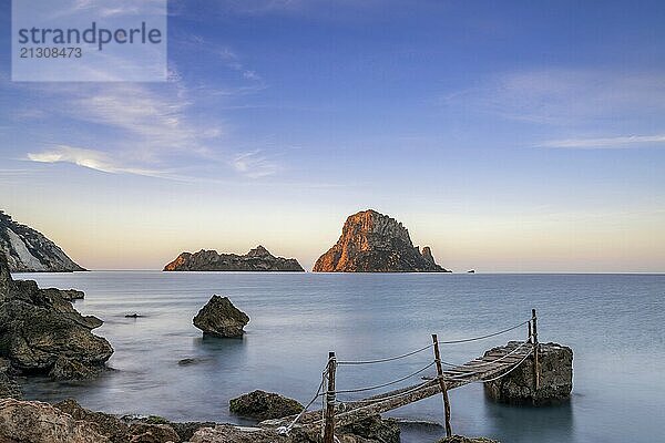 A small wooden pier in Cala d'Hort with a view of the Es Vedra rocks in the background at sunrise