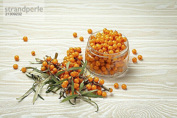 Sea buckthorn ripe berries in glass jar and branches with leaves top view on white wooden rustic background  great for skin  heart  vessels and immune system  food photography  food photography