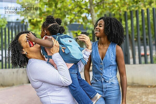 African grandmother embracing her granddaughter and laughing in a park next to her daughter