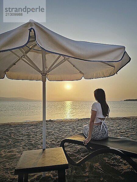 Charming female seated on a lounger at the beach watching the sunrise and taking a morning sunbathe with a view to the sea. Beautiful scene seaside  summer vacation relaxation and holiday relish