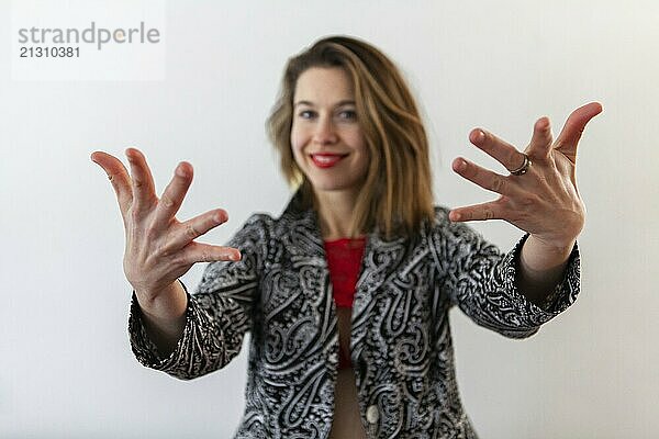 A front portrait of a confident feminist standing against a white background. Smiling fashionable girl with brown hair holds her hands out towards the camera