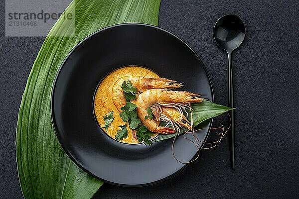 Food  Seafood cream soup with shrimps decorated with tropical leaves. In black plate  on black background. Top view  copy space