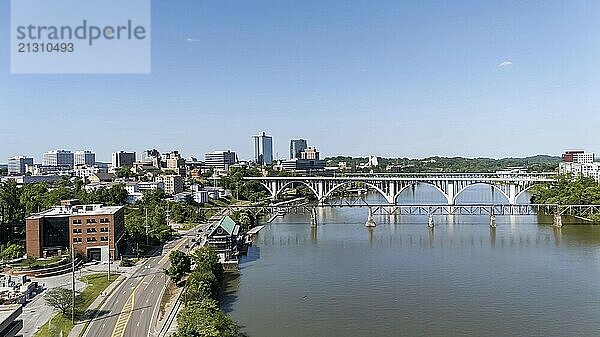 An aerial view of Knoxville  Tennessee reveals a vibrant cityscape with a mix of historic and modern buildings  the Tennessee River weaving through downtown  lush green parks  and the distant Smoky Mountains framing the horizon