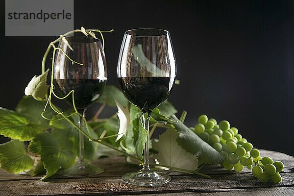 Glass of red wine with bottle and bunch of sour grapes on a black background