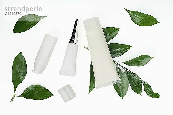 Flat lay view at white cosmetic bottles and containers with green leaves on white table