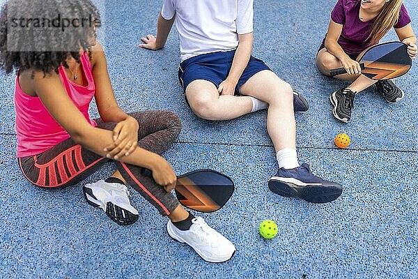 Latin woman and friends talking sitting on a pickelball court after playing together